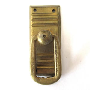 Puede incluir: Un tirador de puerta de latón con forma rectangular redondeada y un pomo decorativo. El tirador tiene un diseño acanalado en la placa posterior.