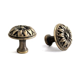 Peut inclure: Deux boutons de meuble en bronze antique avec un motif floral. Les boutons ont une face ronde et texturée et une tige courte et cylindrique. La finition est d'une couleur bronze vieilli et chaleureux, suggérant une esthétique vintage. Les boutons sont probablement utilisés pour les meubles ou à des fins décoratives.