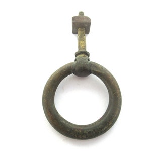 Pode incluir: Uma pega de anel de tração de latão vintage com um acessório de parafuso. A pega é um anel circular com um acabamento ligeiramente desgastado e envelhecido.