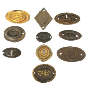 May include: Assortment of 10 antique brass keyhole escutcheons with various designs, including floral, geometric, and ornate patterns. The escutcheons are in various shades of brass, ranging from light gold to dark brown.