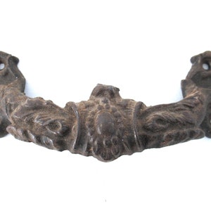 May include: A cast iron drawer pull with an ornate design. The pull is dark brown and has a decorative centre piece.