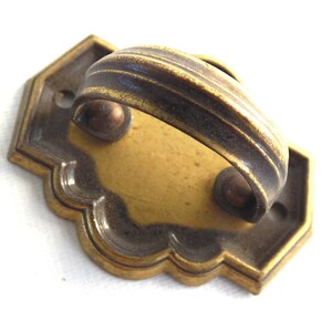 May include: A brass cabinet pull with a decorative, scalloped edge and a curved handle. The handle has a dark patina.