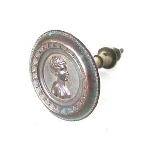 May include: A vintage bronze door knob with a raised profile of a woman's face in a circular design.