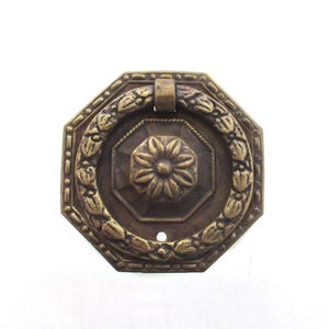 May include: Octagonal brass cabinet pull with a ring handle and a floral design. The pull has a distressed finish and a decorative border.