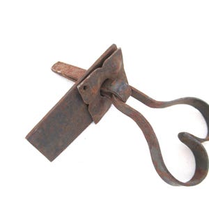 May include: A rusty metal door latch with a heart-shaped handle. The latch is made of two pieces, one with a flat plate and the other with a curved handle. The handle is attached to the plate with a hinge.