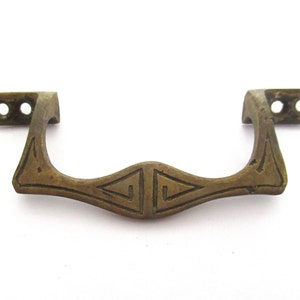 May include: A brass door pull with a decorative geometric design. The pull has two holes on each side for mounting.