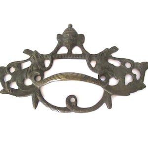 Puede incluir: Un tirador de puerta de estilo antiguo adornado con un diseño estilizado decorativo. El tirador está hecho de metal y tiene un acabado oscuro envejecido.