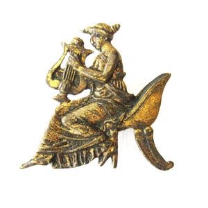 Könnte beinhalten: Eine goldfarbene Metallbrosche, die eine Figur zeigt, die eine Leier spielt. Die Figur sitzt auf einem geschwungenen Sockel und trägt eine fließende Robe.