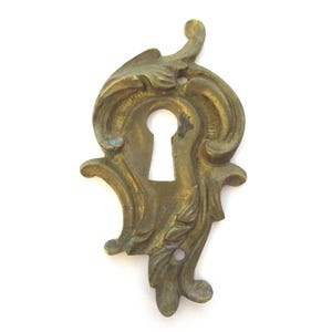 以下が含まれることがあります： 装飾的な真鍮製の鍵穴カバー、フローラルデザイン。 アンティーク調の装飾板は中央に鍵穴があり、周囲には装飾的な装飾が施されています。 真鍮はわずかに古びた風合いです。