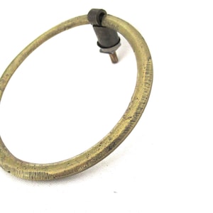 Könnte beinhalten: Ovaler Schubladengriff aus Messing mit strukturierter Oberfläche. Der Griff hat ein dunkles Metallbefestigungsteil und einen Gewindestift zur Befestigung. Das Messing hat ein leicht gealtertes Aussehen, was auf Vintage-Ursprünge hindeutet. Ideal für Möbelrestaurierung.