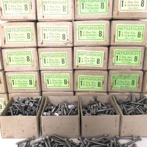 Könnte beinhalten: Eine Sammlung von 12 Schachteln mit Schrauben, jede mit der Aufschrift "Nettlefolds 1 One Gro. 4 Screws 8". Die Schachteln sind in drei Reihen zu vier angeordnet. Im Vordergrund befinden sich auch vier kleine Schachteln mit Schrauben.