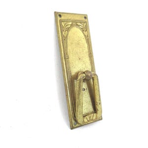 以下が含まれることがあります： 装飾的なデザインが施された金色の金属製のドアノブ。ノブは、アーチ型の装飾と花柄が施された長方形のプレートに取り付けられています。