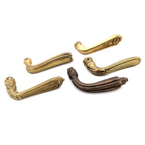 Op de afbeelding: Vijf antieke deurgrepen in verschillende stijlen. De grepen zijn gemaakt van messing en hebben ingewikkelde details. Sommige grepen zijn goudkleurig, terwijl andere een donkerder messing hebben.