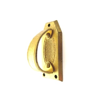 Może przedstawiać: Złoty metalowy klamka do drzwi z ozdobnym owalnym wzorem i zakrzywionym uchwytem. Klamka ma cztery otwory montażowe.
