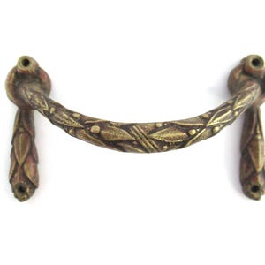 Op de afbeelding: Een messing deurgreep met een decoratief bladontwerp. De greep is gebogen en heeft een gladde, gepolijste afwerking.