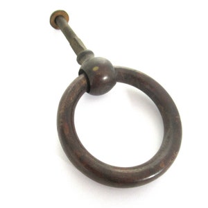 Può includere: Una maniglia a anello in metallo marrone scuro con un pomo rotondo e una vite. La maniglia è progettata per l'uso su una porta o un cassetto.