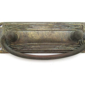 Peut inclure: Poignée de tiroir en laiton antique avec un motif décoratif et une poignée incurvée.