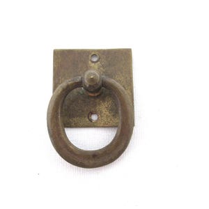 Op de afbeelding: Een messing ringtrekhengsel met een vierkante basis. Het handvat is bevestigd aan een vierkante plaat met twee zichtbare schroeven.