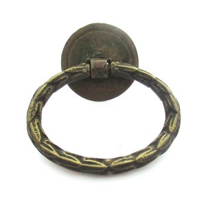 Könnte beinhalten: Ein Messing-Ringzug mit einem dekorativen Blattdesign. Der Ringzug hat eine runde, flache Basis.