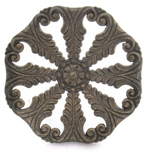 Puede incluir: Un adorno metálico decorativo con un diseño circular que presenta intrincados patrones florales. El adorno está hecho de un metal oscuro envejecido con un acabado dorado.