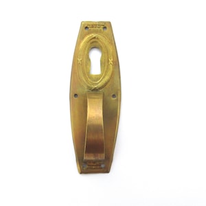 May include: A brass door handle with a keyhole and a decorative design. The handle is oval shaped and has a raised edge.