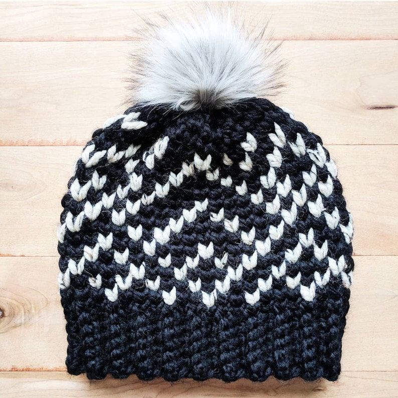 May include: Black and white crocheted beanie with a white pom pom on top. The beanie has a chevron pattern.