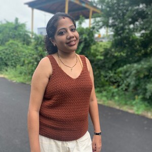 Peut inclure: Une femme portant un d&eacute;bardeur en crochet marron et un pantalon blanc. Elle a un point rouge sur le front et sourit &agrave; la cam&eacute;ra.