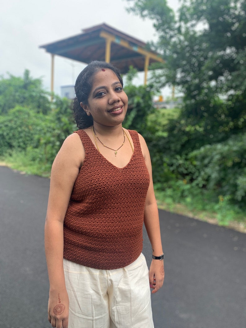 Peut inclure: Une femme portant un d&eacute;bardeur en crochet marron et un pantalon blanc. Elle a un point rouge sur le front et sourit &agrave; la cam&eacute;ra.