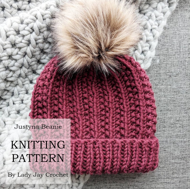 May include: A burgundy knitted beanie with a faux fur pom pom. The beanie is made with a textured stitch and has a ribbed brim. The beanie is called "Justyna Beanie" and the knitting pattern is by "Lady Jay Crochet".