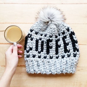 Puede incluir: Un gorro de punto gris y negro con un pomp&oacute;n blanco en la parte superior. El gorro tiene un patr&oacute;n de rayas blancas y negras.
