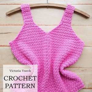 Peut inclure: Un patron de crochet pour un d&eacute;bardeur rose, suspendu &agrave; un cintre en bois. Le patron s'appelle "Victoria Vneck Crochet Pattern" par "Lady Jay Crochet".