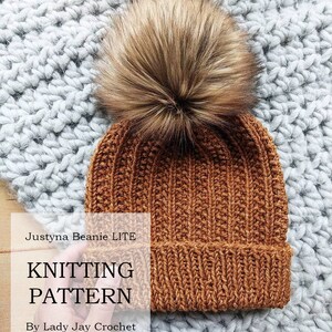 May include: A brown knitted beanie with a faux fur pom pom. The beanie has a ribbed texture and is on a gray fuzzy surface. The text "Justyna Beanie LITE KNITTING PATTERN By Lady Jay Crochet" is on a white rectangle.