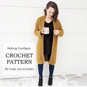 Puede incluir: Un cárdigan de crochet amarillo mostaza con un frente largo y abierto. El cárdigan se lleva sobre una camisa negra y unos vaqueros azules. El texto "Solveig Cardigan CROCHET PATTERN By Lady Jay Crochet" es visible en la imagen.