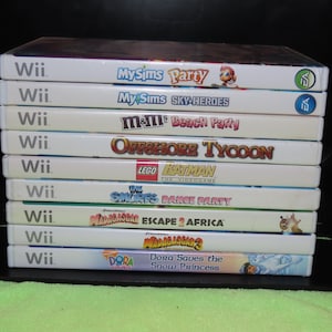 May include: A stack of ten video game cases for the Wii console. The games include MySims Party, MySims Sky Heroes, M&M's Beach Party, Offshore Tycoon, Lego Batman: The Videogame, The Smurfs Dance Party, Madagascar Escape 2 Africa, Madagascar 3, and Dora Saves the Snow Princess.