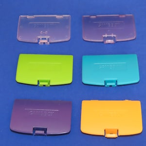 May include: Six different coloured Game Boy Color game cartridge covers. The covers are translucent and have the Game Boy Color logo printed on them. The colours are pink, green, blue, purple, and orange.
