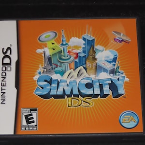 May include: A Nintendo DS game cartridge for SimCity DS. The game cover features a bright orange background with a 3D rendering of the game title in blue and white. The cover also features a variety of iconic landmarks from around the world, including the Eiffel Tower, the Sydney Opera House, and Big Ben.