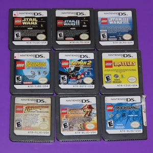 May include: A collection of nine Nintendo DS game cartridges featuring LEGO themes, including Star Wars, Batman, Indiana Jones, and Rock Band. The cartridges are arranged in three rows of three, with the titles visible on each cartridge.