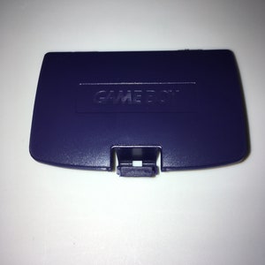 May include: A purple Game Boy Color game cartridge case with the words "GAME BOY" embossed on the top.