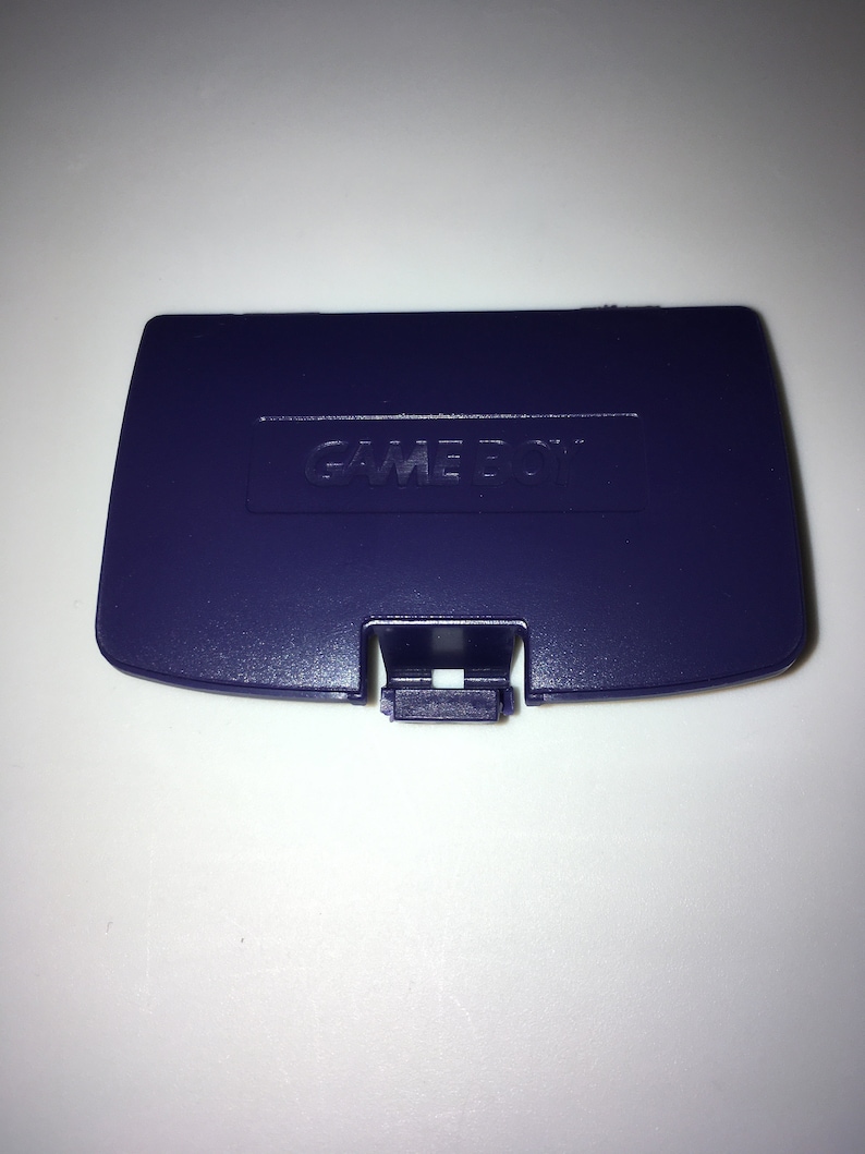 May include: A purple Game Boy Color game cartridge case with the words "GAME BOY" embossed on the top.