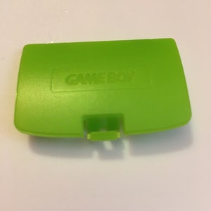 May include: A bright green Game Boy Color game cartridge case with the words "GAME BOY" embossed on the top.