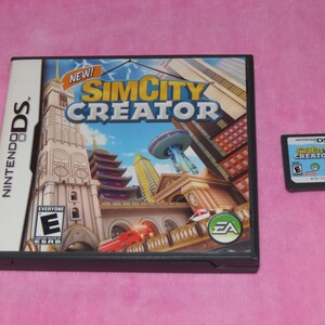 May include: A Nintendo DS game case and cartridge for "SimCity Creator." The case features a colorful cityscape with the game title and "NEW!" text. The cartridge is small and rectangular, with the game title and rating.