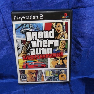 May include: A PlayStation 2 video game case for Grand Theft Auto: Liberty City Stories. The case features a comic book style design with multiple characters and a red car.