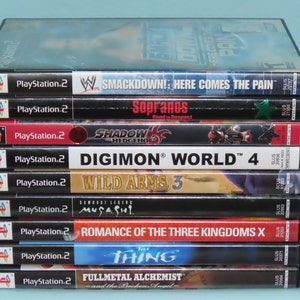 May include: A stack of ten PlayStation 2 video game cases. The games include Smackdown: Here Comes the Pain, The Sopranos: Road to Respect, Shadow the Hedgehog, Digimon World 4, Wild Arms 3, Samurai Legend Musashi, Romance of the Three Kingdoms X, The Thing, and Fullmetal Alchemist: and the Broken Angel.