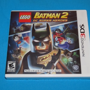 May include: A white Nintendo 3DS game case with a colorful image of Lego Batman 2: DC Super Heroes. The game features a Lego version of Batman in the foreground, with other Lego characters like Superman, Robin, and the Joker in the background. The game is rated E for Everyone 10+ by the ESRB.