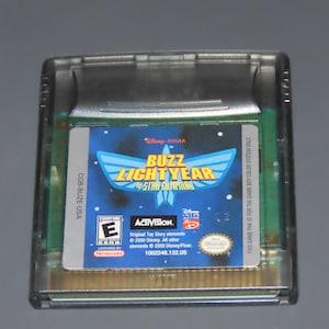 May include: A clear plastic Game Boy Color cartridge featuring the game "Buzz Lightyear of Star Command." The game's label is blue with a stylized Buzz Lightyear graphic and the Disney/Pixar logo. The cartridge has a gold-colored connector.