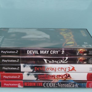 May include: A stack of five PlayStation 2 video game cases. The top case is for Devil May Cry 2, the next case is for Devil May Cry 2, the third case is for Devil May Cry 3, the fourth case is for Devil May Cry 2 Special Edition, and the bottom case is for Resident Evil Code: Veronica X.