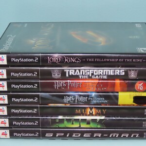 May include: A stack of seven PlayStation 2 video game cases. The games are: The Lord of the Rings: The Fellowship of the Ring, Transformers: The Game, Harry Potter and the Goblet of Fire, Harry Potter and the Prisoner of Azkaban, The Mummy: Returns, The Hulk, and Spider-Man.