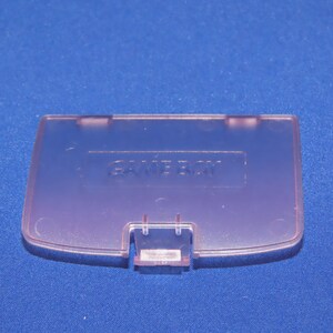May include: A translucent purple Game Boy Color game cartridge case with the word "GAME BOY" embossed on the top.