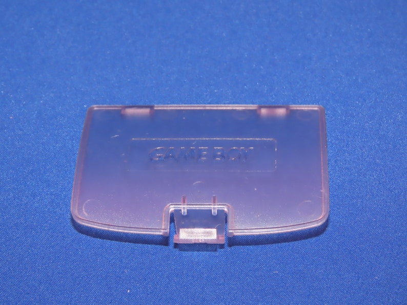 May include: A translucent purple Game Boy Color game cartridge case with the word "GAME BOY" embossed on the top.