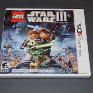 May include: A Nintendo 3DS game cartridge for Lego Star Wars III: The Clone Wars. The front of the cartridge features a colorful image of Lego characters from the Star Wars franchise, including Yoda, Obi-Wan Kenobi, and Anakin Skywalker. The game is playable in both 2D and 3D.